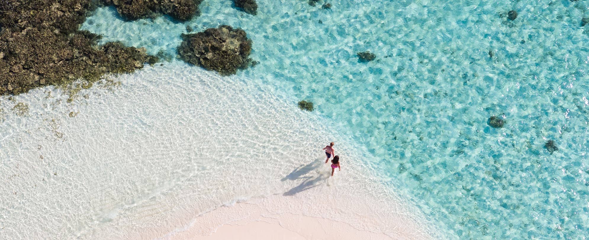 Bird's eye view of couple walking into crystal clear ocean water