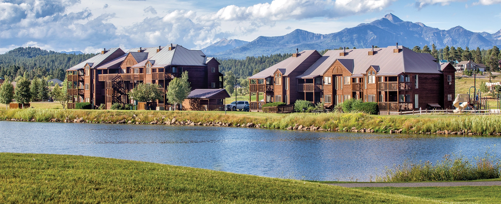 The exterior of WorldMark/Club Wyndham Pagosa, a Colorado timeshare resort surrounded by a lake and mountains.